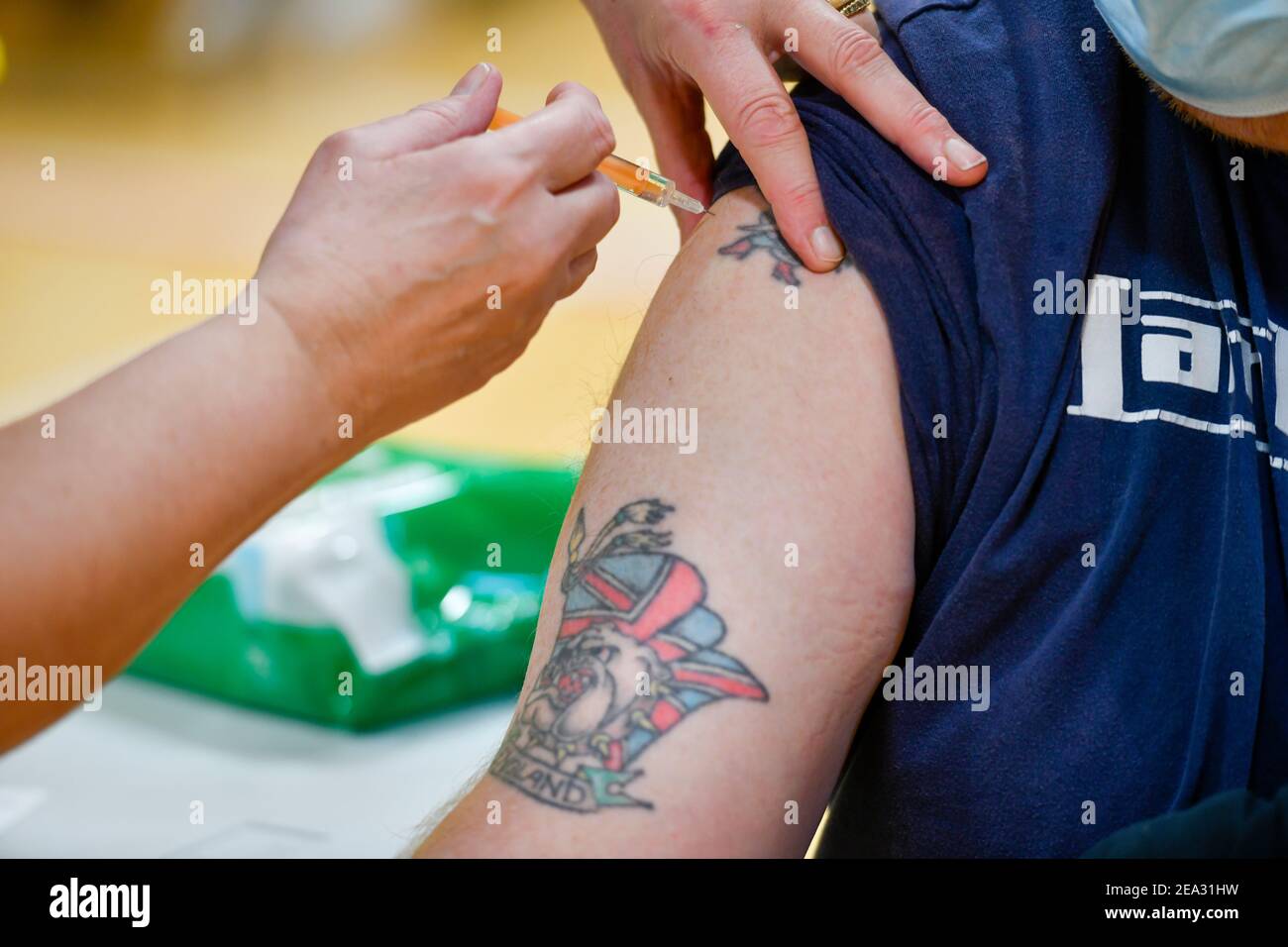 A man with a union flag tattoo featuring a bulldog and the word England receives his Covid-19 vaccine. A Covid19 vaccination session held at Workington Leisure Centre in Cumbria using the Oxford Astra Zeneca vaccine. The cohort being given the vaccine are those over 70 years-old along with younger people who had been shielding or were clinically extremely vulnerable. The Workington Primary Care Network relocated from the town's surgeries to the larger space of the leisure centre to speed up the vaccine delivery: 6 February 2021 STUART WALKER  Stuart Walker Photography 2021 Stock Photo