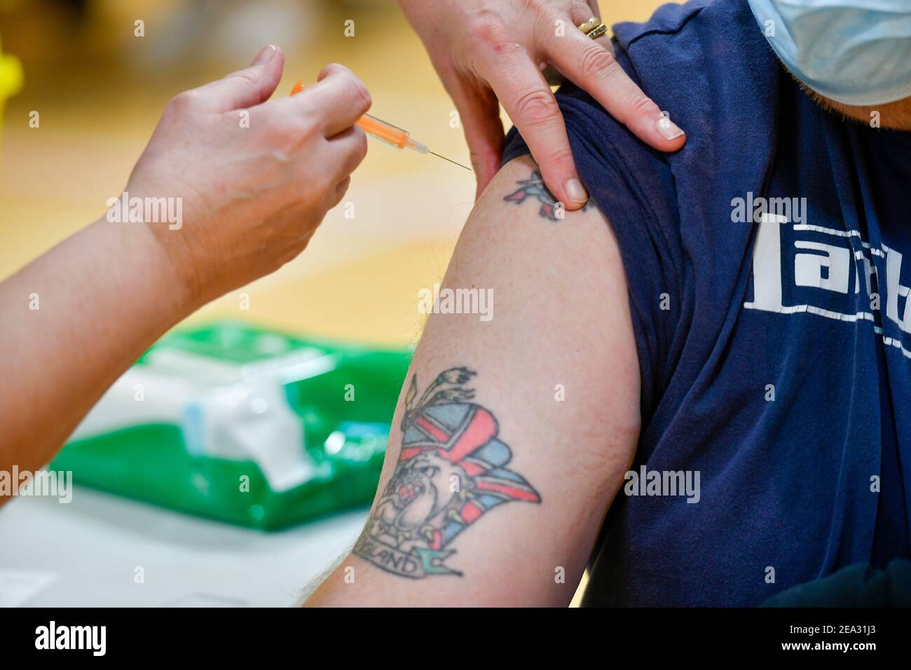 A man with a union flag tattoo featuring a bulldog and the word England receives his Covid-19 vaccine. A Covid19 vaccination session held at Workington Leisure Centre in Cumbria using the Oxford Astra Zeneca vaccine. The cohort being given the vaccine are those over 70 years-old along with younger people who had been shielding or were clinically extremely vulnerable. The Workington Primary Care Network relocated from the town's surgeries to the larger space of the leisure centre to speed up the vaccine delivery: 6 February 2021 STUART WALKER  Stuart Walker Photography 2021 Stock Photo