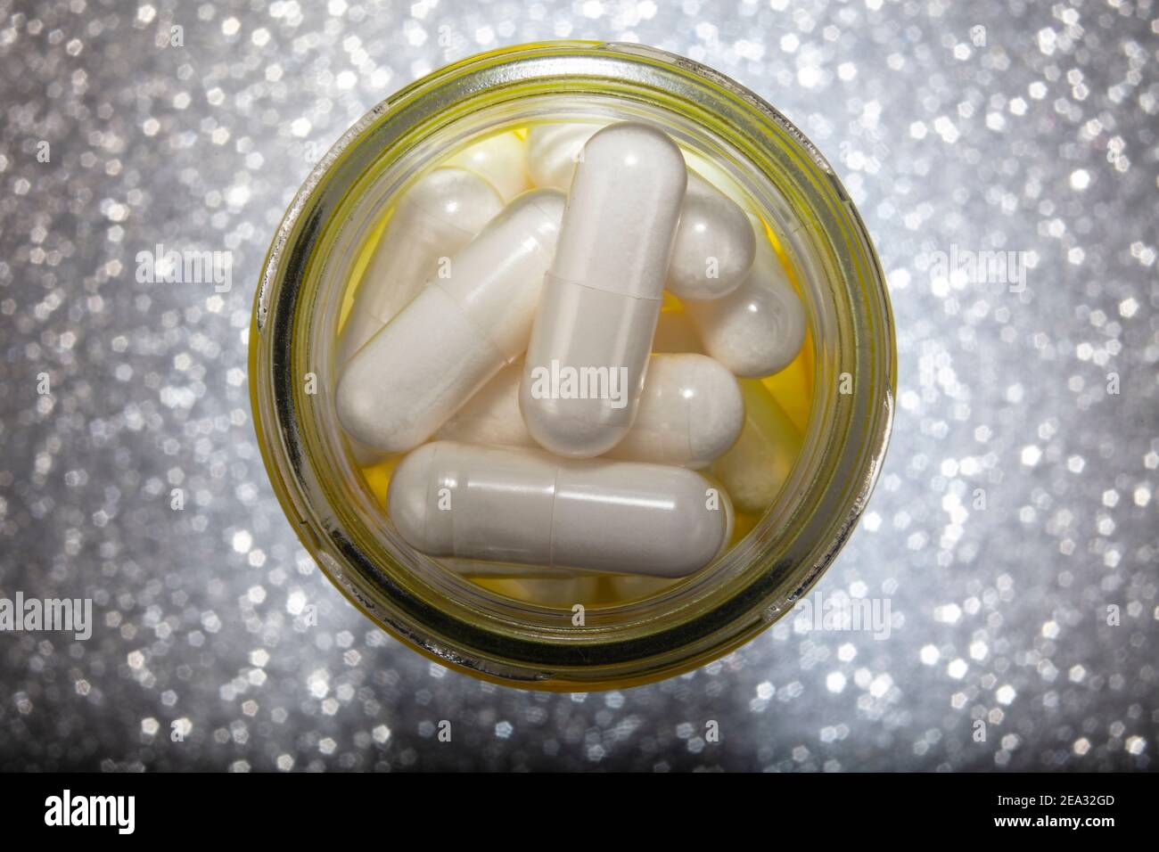 Macro Photo of White Pills In Yellow Glass Jar. Close up  Photo of  Pills  On Silver Pentagram Bokeh Background. With Copy Space. Stock Photo