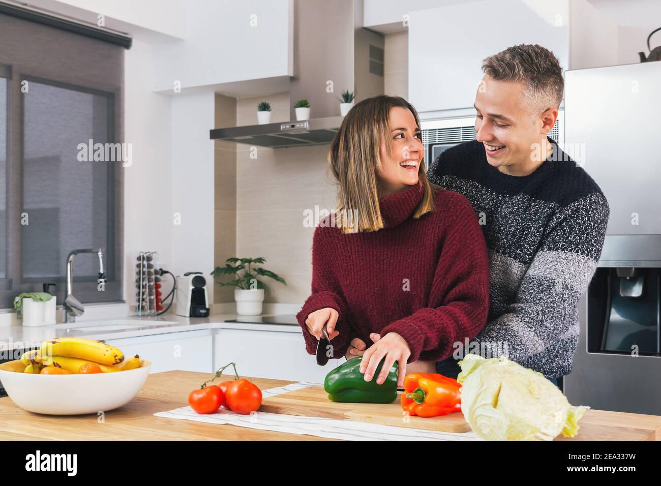 Portrait of happy young couple in love cooking vegan food together in a modern kitchen. Preparing healthy meal, cutting vegetables Stock Photo