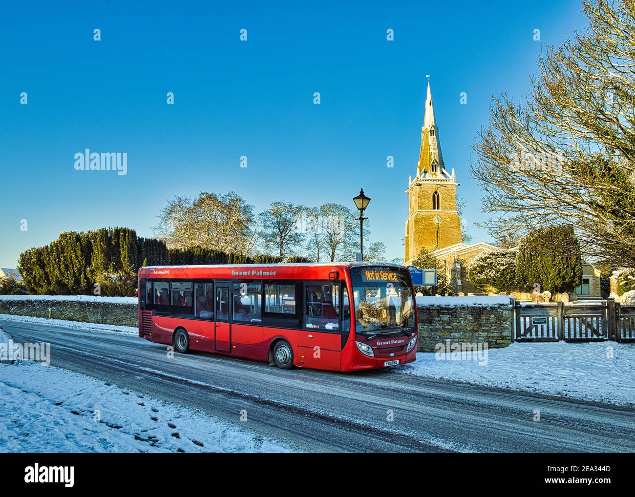 A red bus parked in snow at St Peter's village church, Sharnbrook, Bedfordshire, England, UK Stock Photo