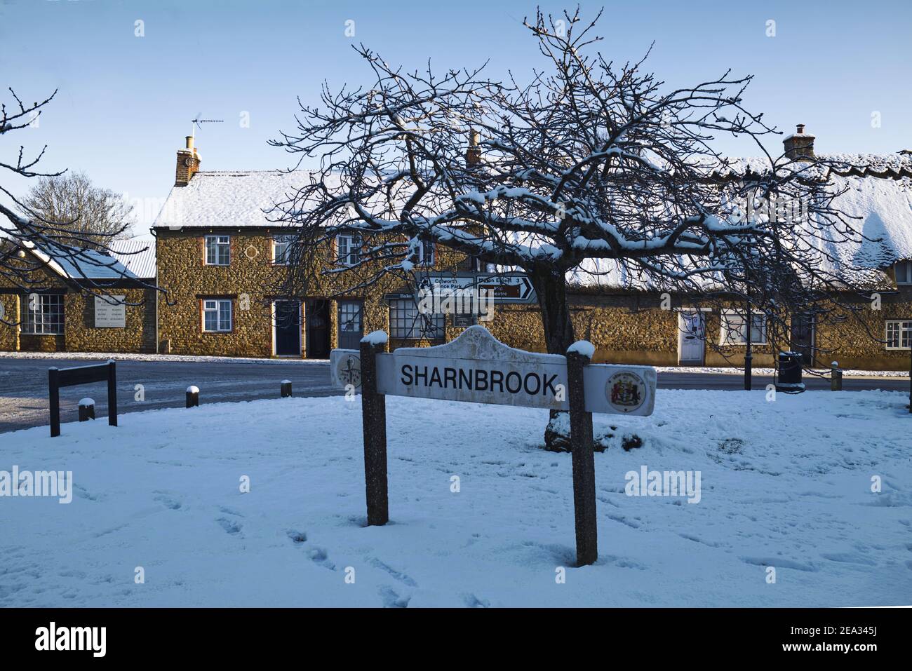 Sharnbrook, Bedfordshire, England, UK - Winter scene after snow with village sign on the green surrounded by thatched cottages Stock Photo
