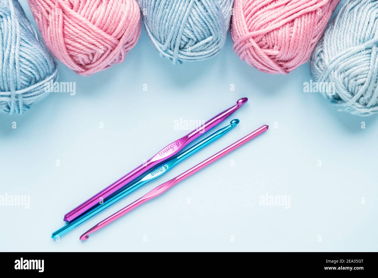 Multicolored crochet hooks with balls of yarn on a blue background. Stock Photo