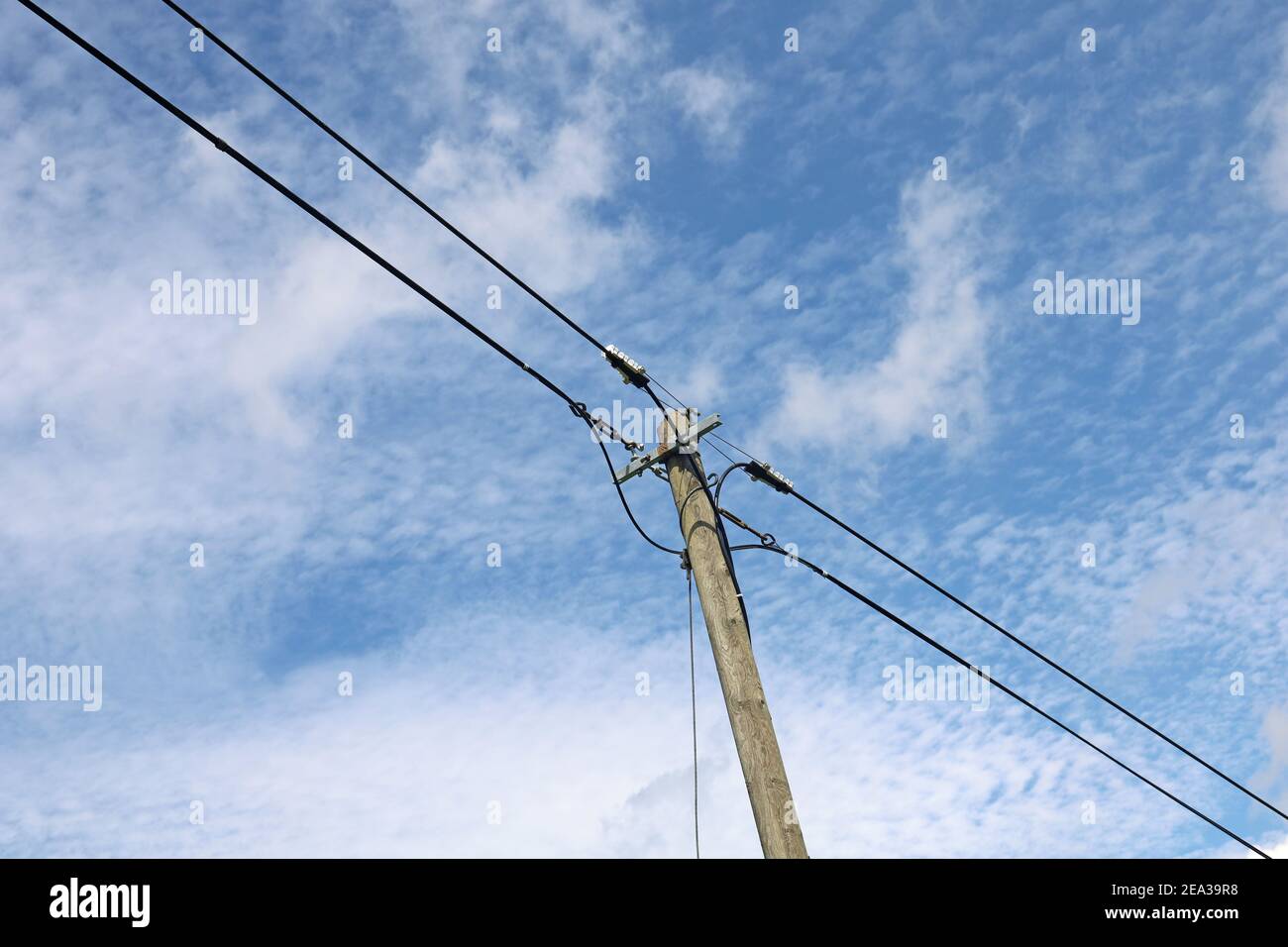 Old wooden power pole with power lines against blue cloudy sky Stock Photo