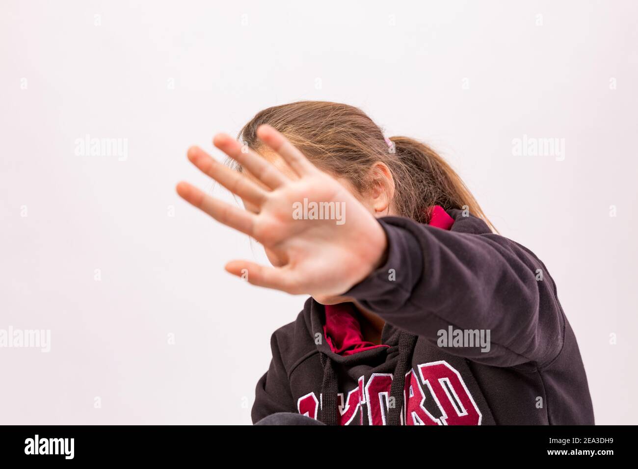 Young girl who denies being photographed shielding her face with hand in foreground Stock Photo