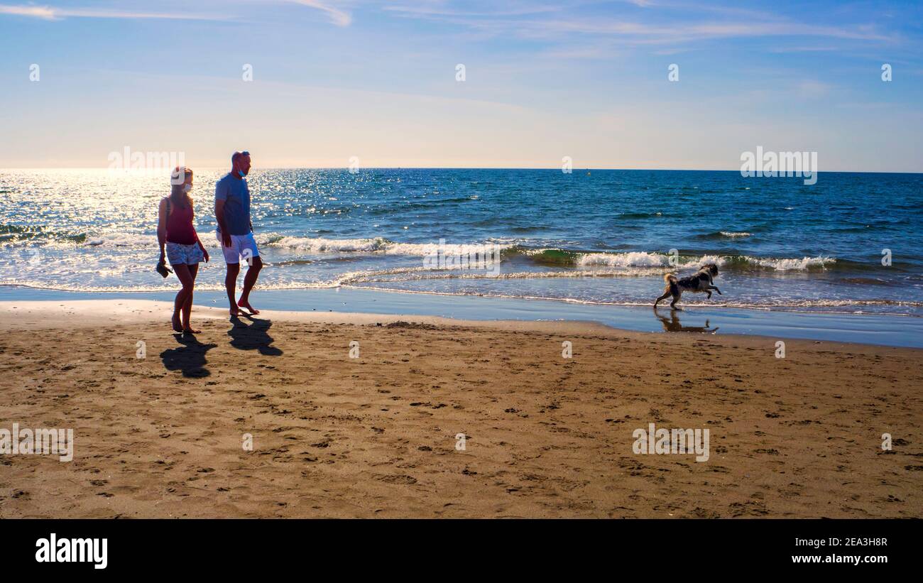Marbella, Malaga, Spain.  October 2020.    Tourist couple walking with their dog on a beach in Marbella on a sunny autumn day. Stock Photo