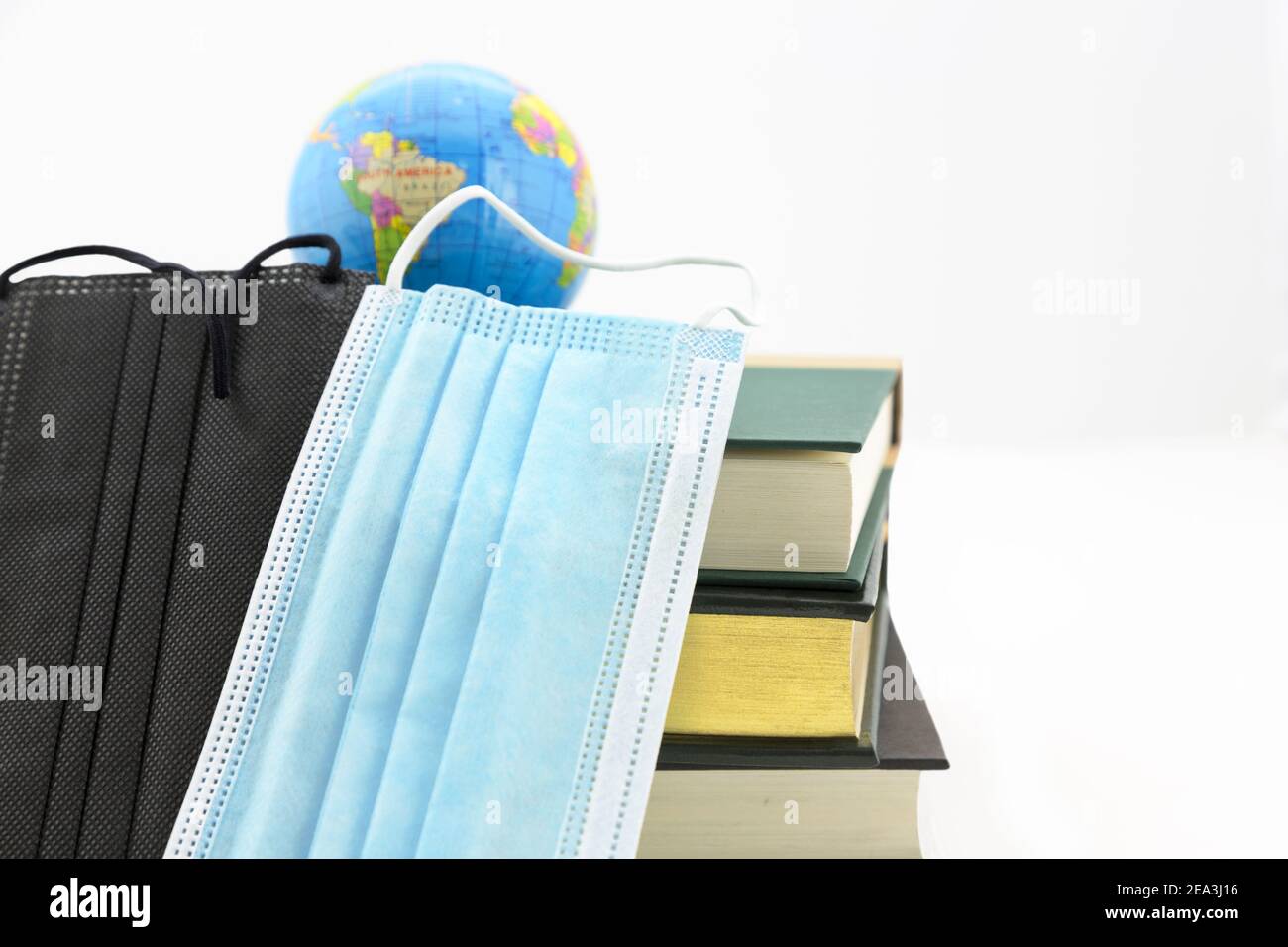 Conceptual still life on worldwide pandemic and global strategic issues seen in symbols of globe, two face masks, and stacked books Stock Photo