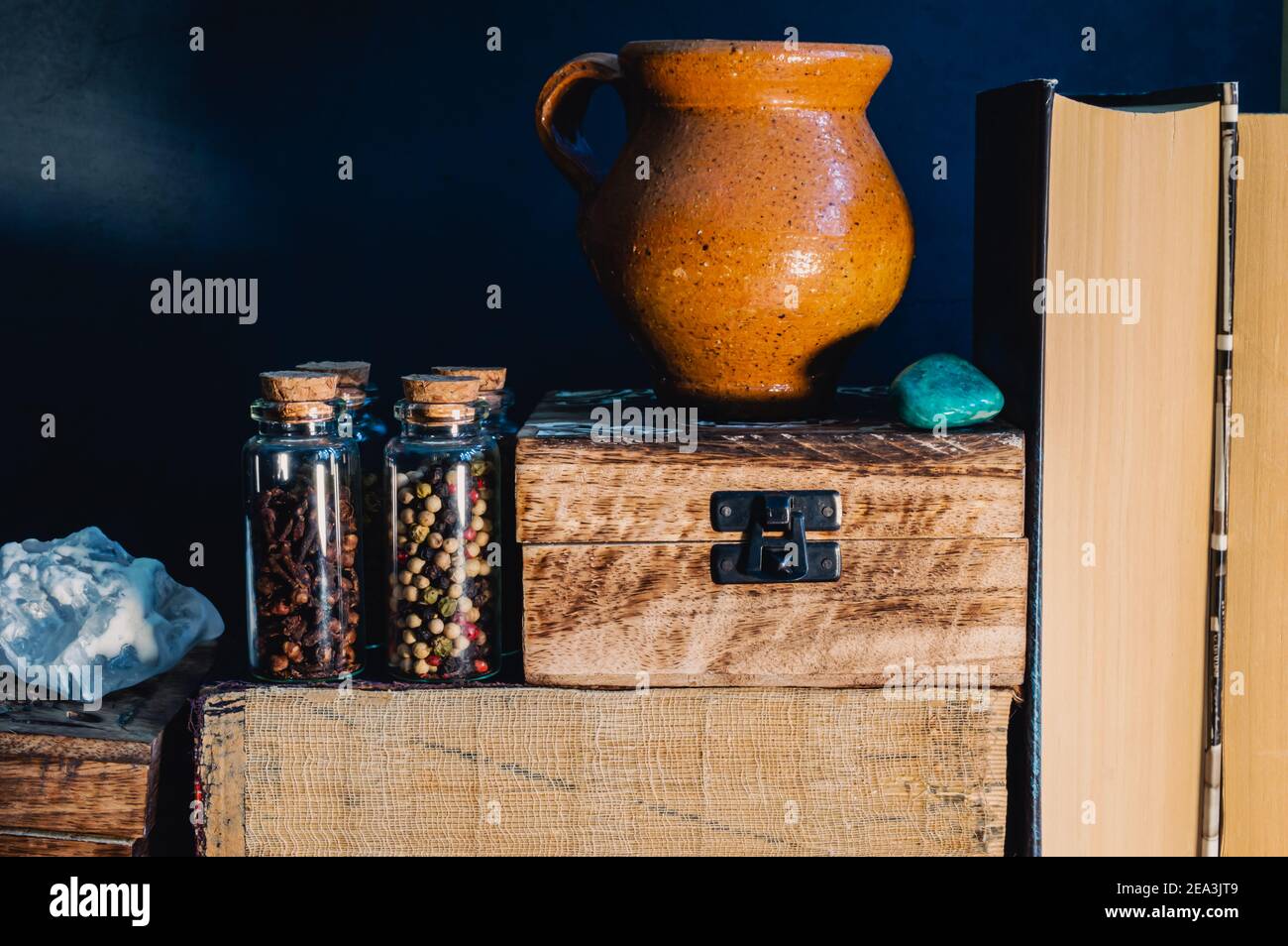 Still life image of books, wooden boxes, glass stopper bottles with spices an earthenware jug and semi precious stones in warm light Stock Photo