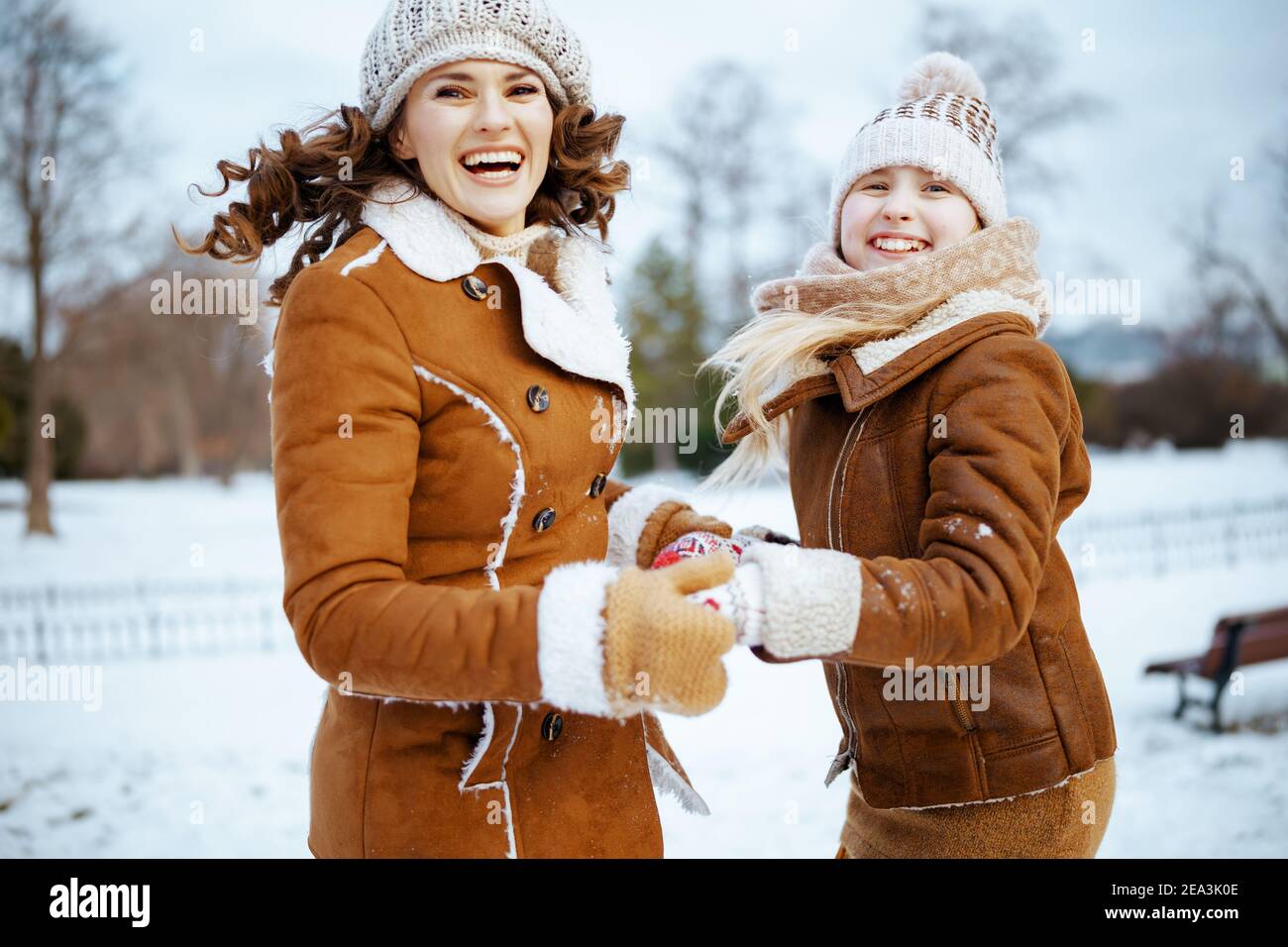 smiling modern mother and child in a knitted hats and sheepskin coats with mittens in a knitted hat and sheepskin coat jumping outside in the city par Stock Photo