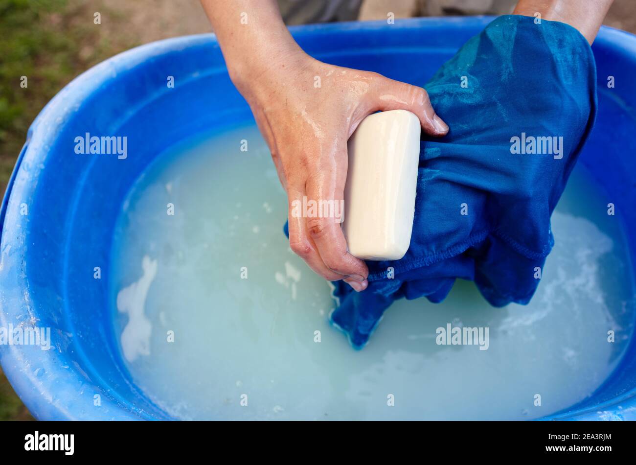 Manual hand washing. Close-up of woman hand washing laundry in blue plastic basin outdoor. Female hands washing clothes in soapy wate Stock Photo