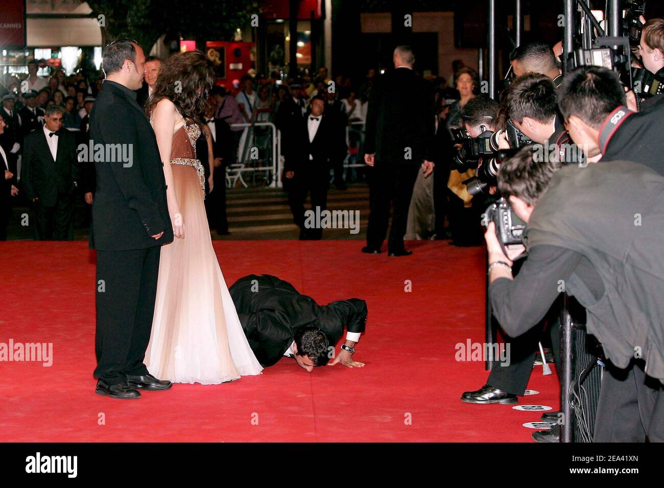 Turkish actor Nazmi Kirik gives a kiss to the red carpet while Iraqi director Hiner Saleem and Turkish actress Belcim Bilgin are watching before the screening of their movie 'Kilometre Zero', during the 58th international Cannes film festival in Cannes, southern France, on May 12, 2005. Photo by Hahn-Nebinger-Klein/ABACA. Stock Photo