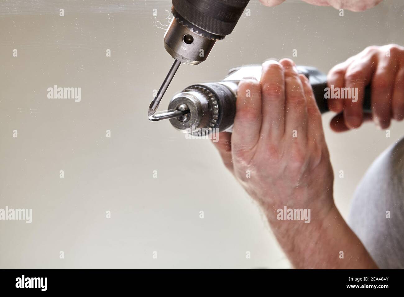 Worker drills hole in surface of mirror using glass drill bit Stock