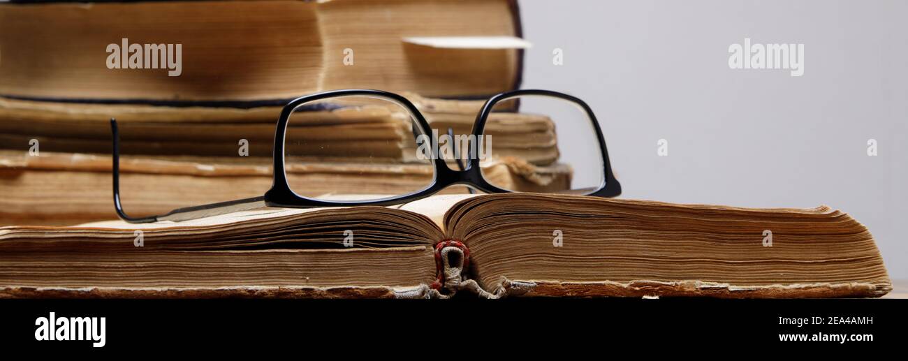 stack of old books with bookmarks on wooden table. glasses lie on an open book. Stock Photo