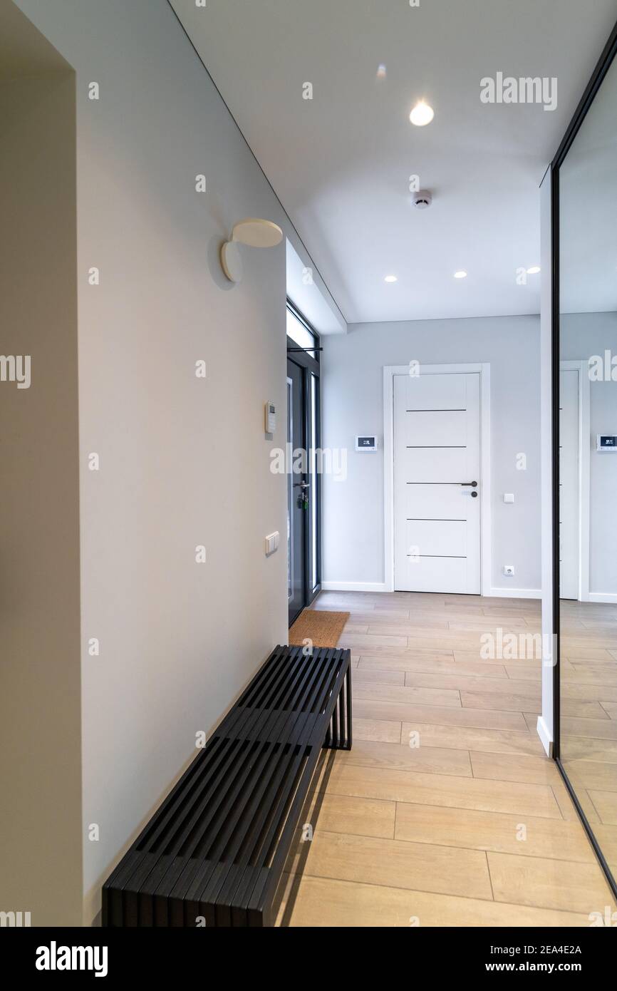 Interior of a spacious bright hallway in a new modern house. Comfortable black bench on one side of the corridor, in front of a sliding door closet wi Stock Photo