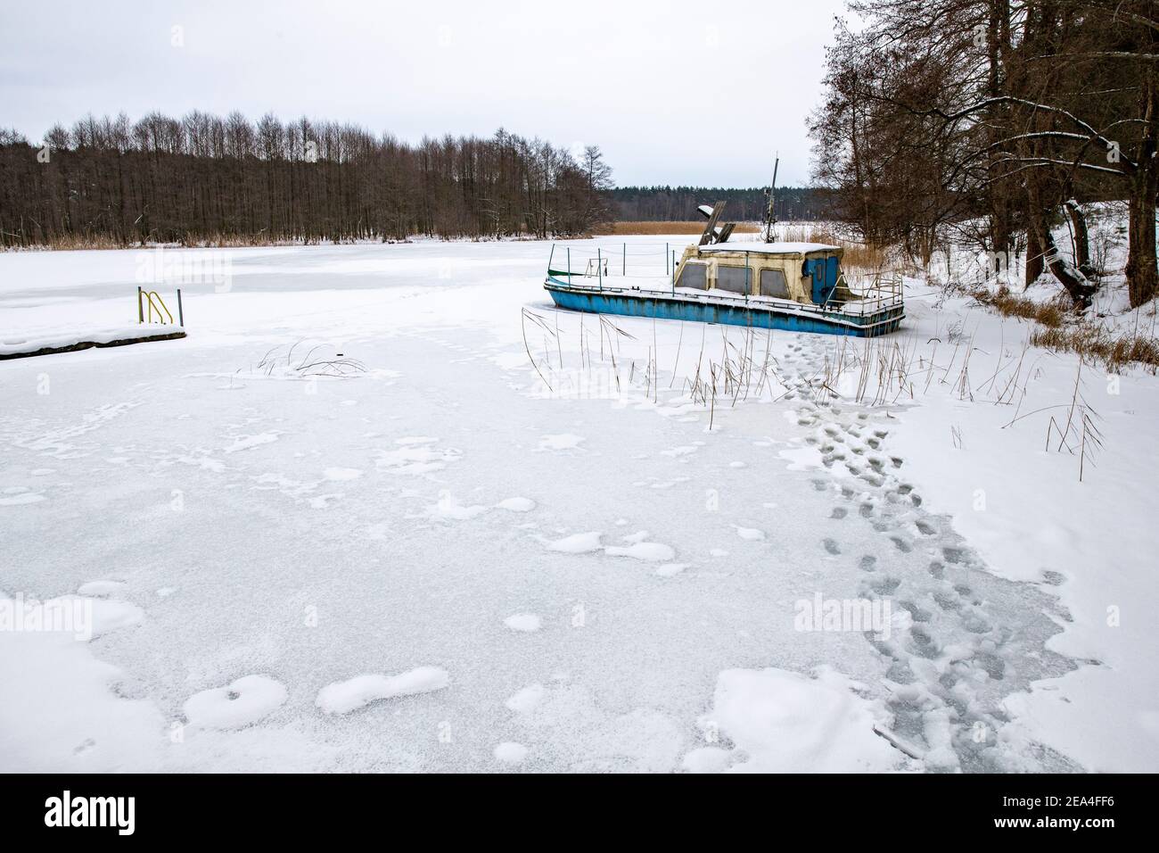 A large boat trapped in ice on a lake. A frozen lake in a boat dock. Winter season. Stock Photo