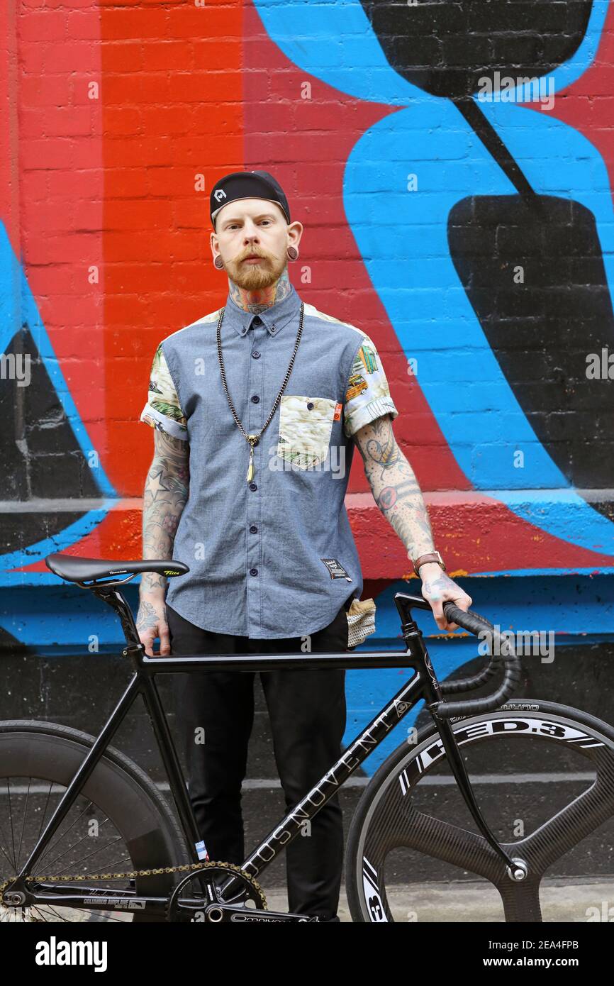 Young hipster man with his bike in front graffiti wall background. Stock Photo