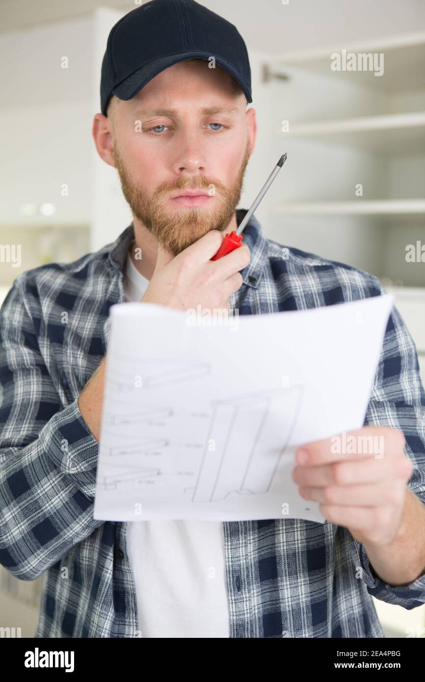 man holding a screwdriver reading furniture assembly instructions Stock