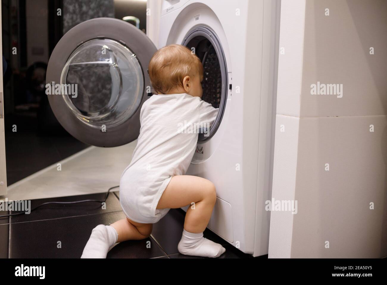 Child climbing into frontloading washing machine. Side view. Lack of