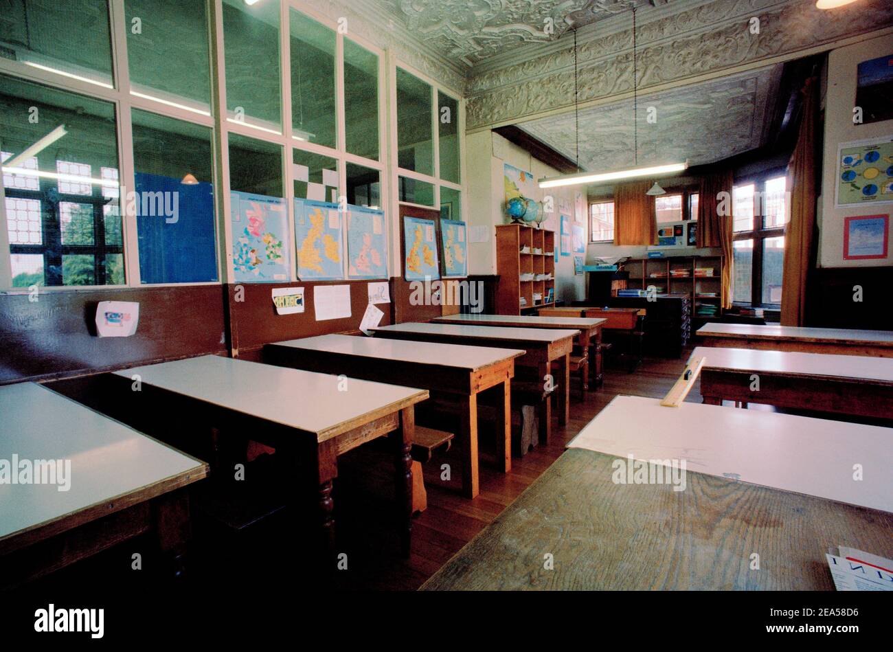Old Empty Classroom with Wooden Desks and Maps on the Walls Stock Photo