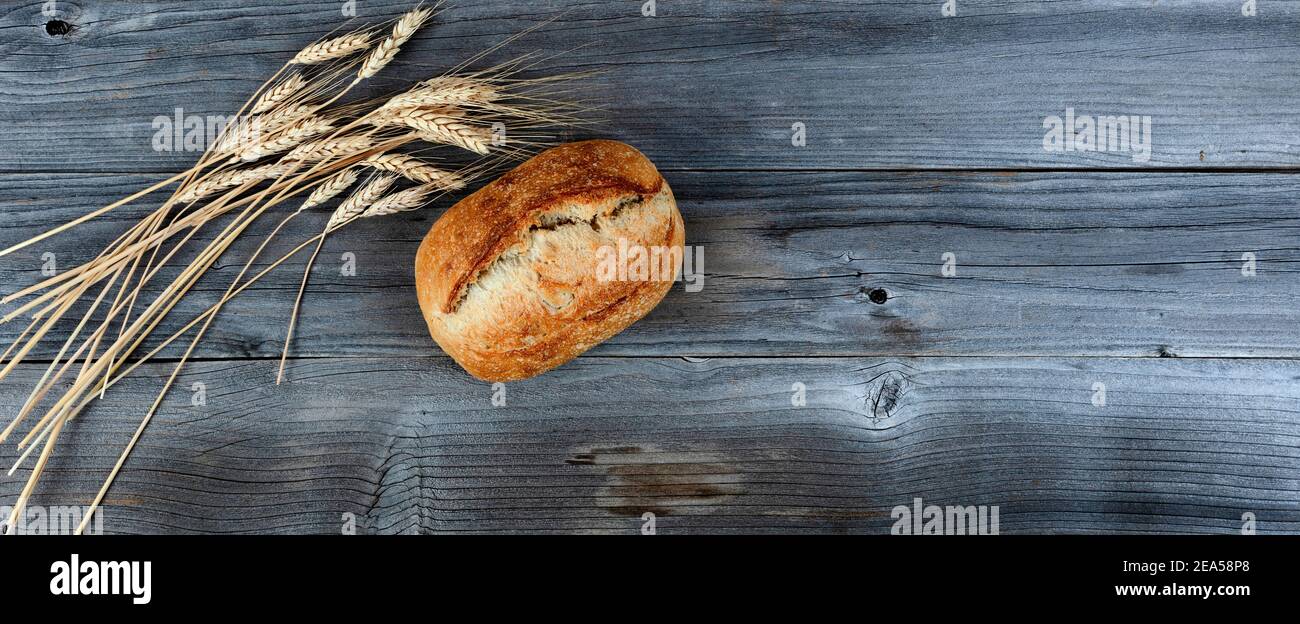 Top view of homemade full sourdough loaf of bread with dried wheat stalks on weathered wooden planks Stock Photo