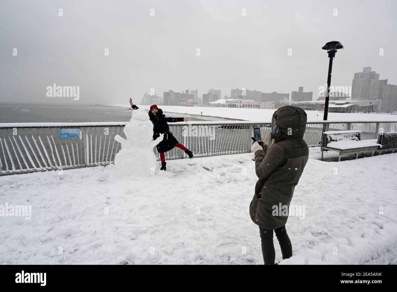 Brooklyn, New York, USA. 07 February 2021, Brooklyn, New York, USA. Woman poses with snowman on pier on Brooklyn's famous Coney Island as New York City experiences its second major winter storm in seven days Credit: Joseph Reid/Alamy Live News Stock Photo