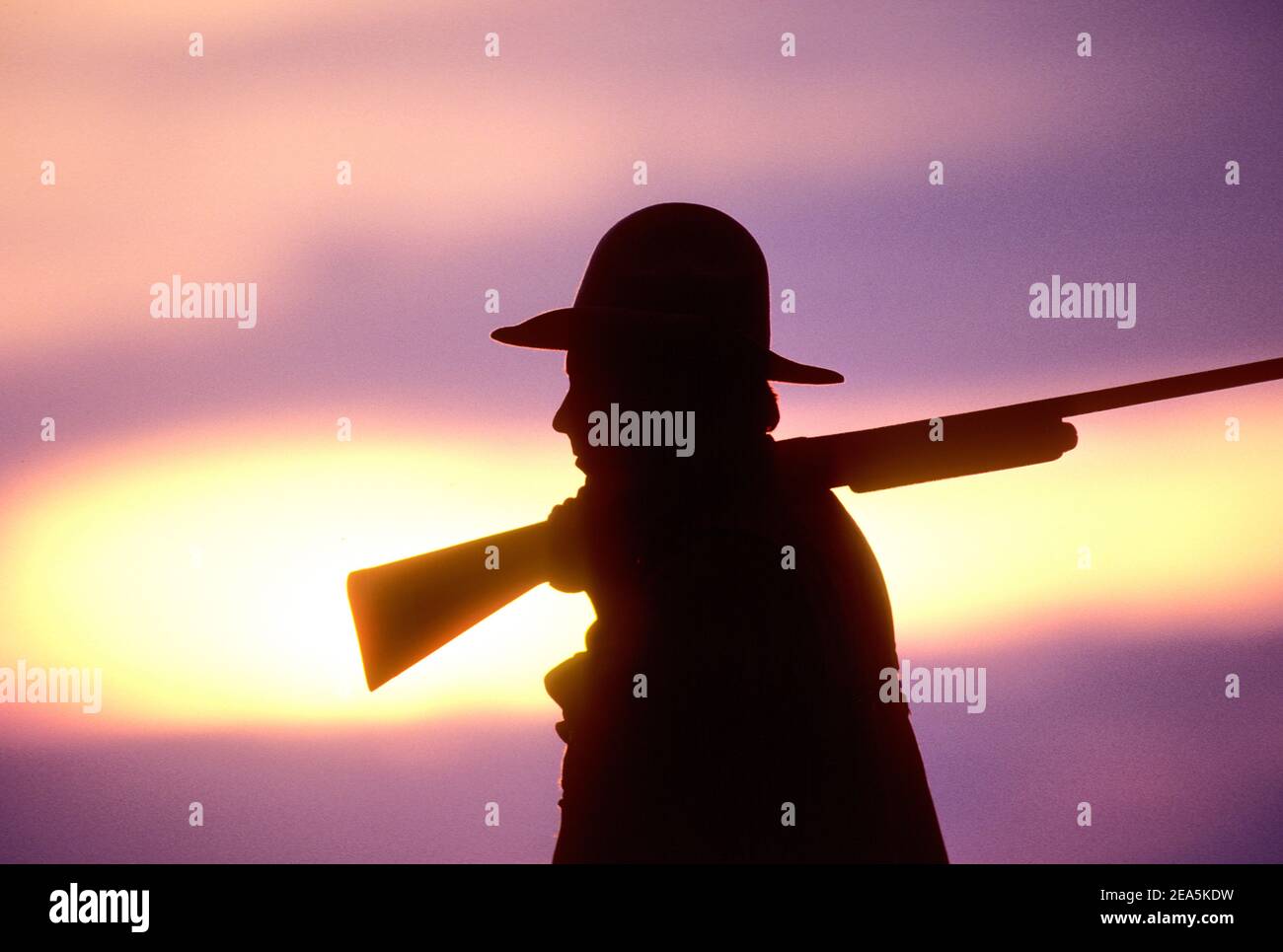 Silhouette of a man holding a shotgun at sunset Stock Photo