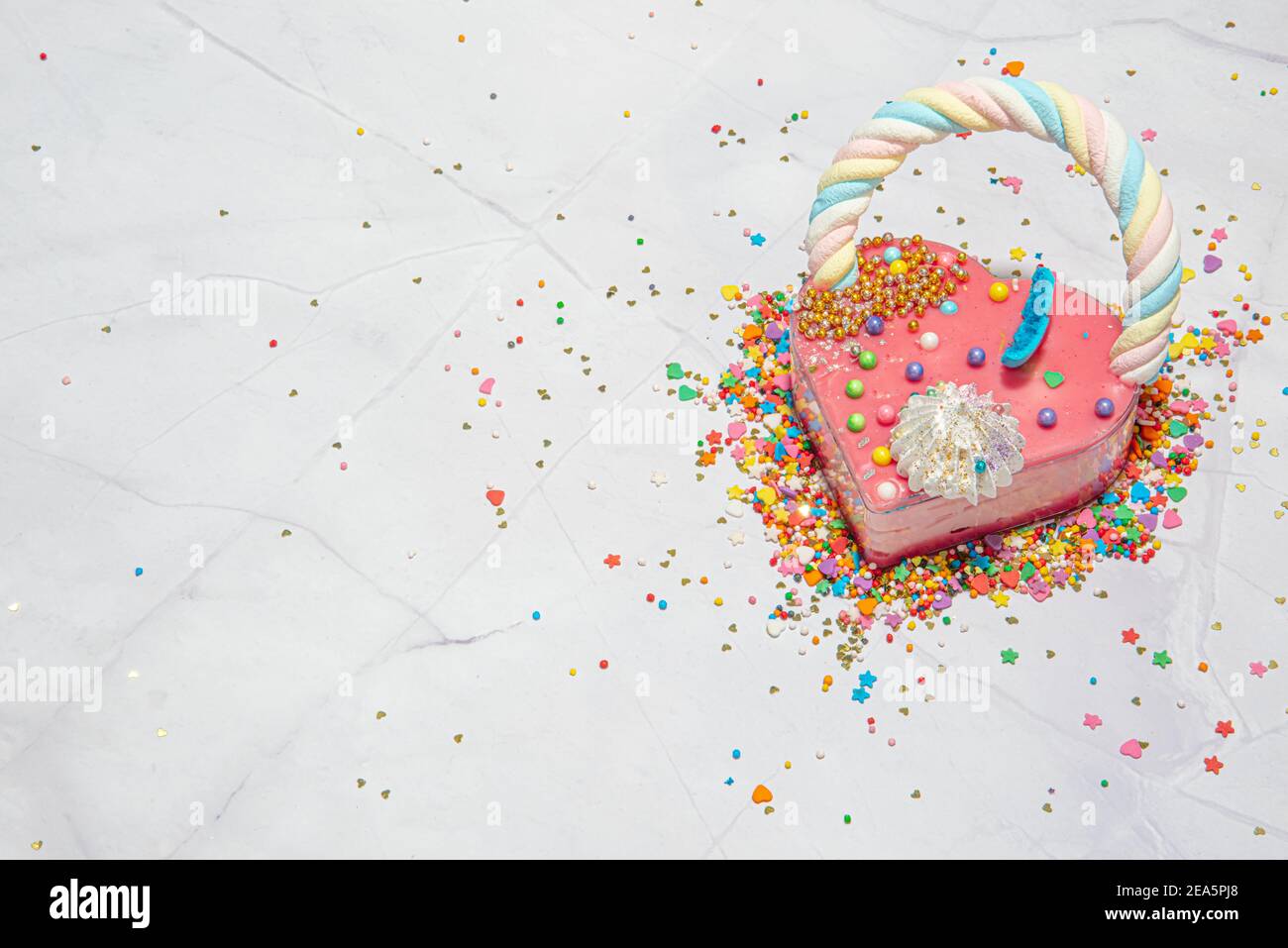 Pink heart shape cake on a white marble background with a lot of small colorful candies. Valentine day. About love. copy space. High quality photo Stock Photo