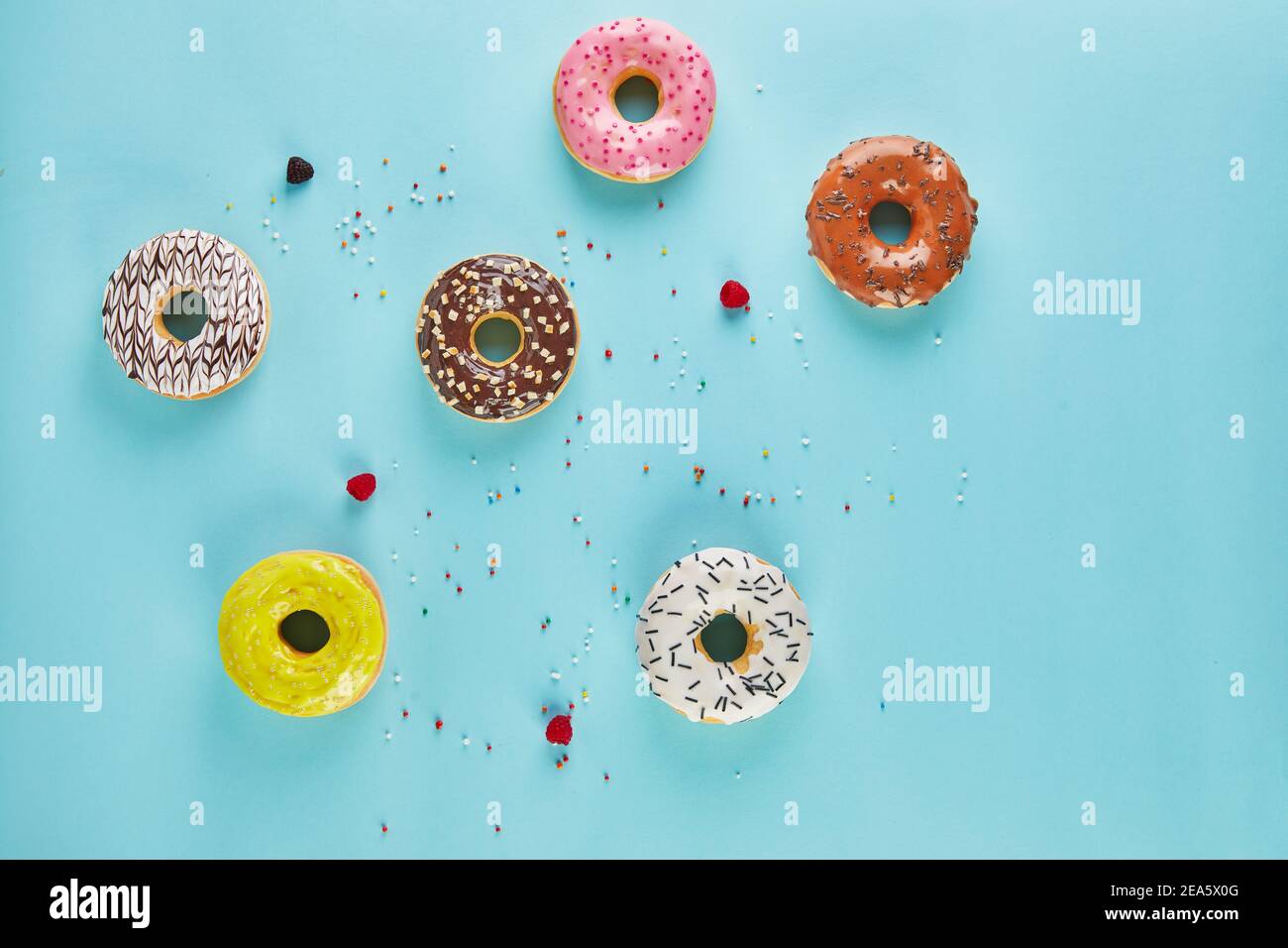 Multicolored donuts with frosting and sprinkles on blue background. Flat lay Stock Photo