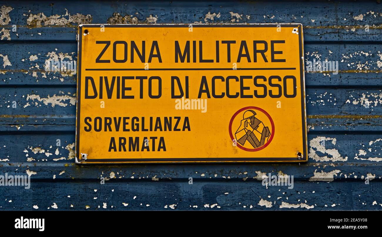 Italian military area with yellow sign: 'Military zone, no entry, armed surveillance'. 'Zona militare, divieto di accesso, sorveglianza armata' Stock Photo