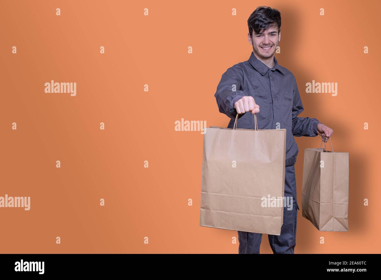 Delivery man with paper bags in his hands delivering the order, dressed in uniform and smiling Stock Photo