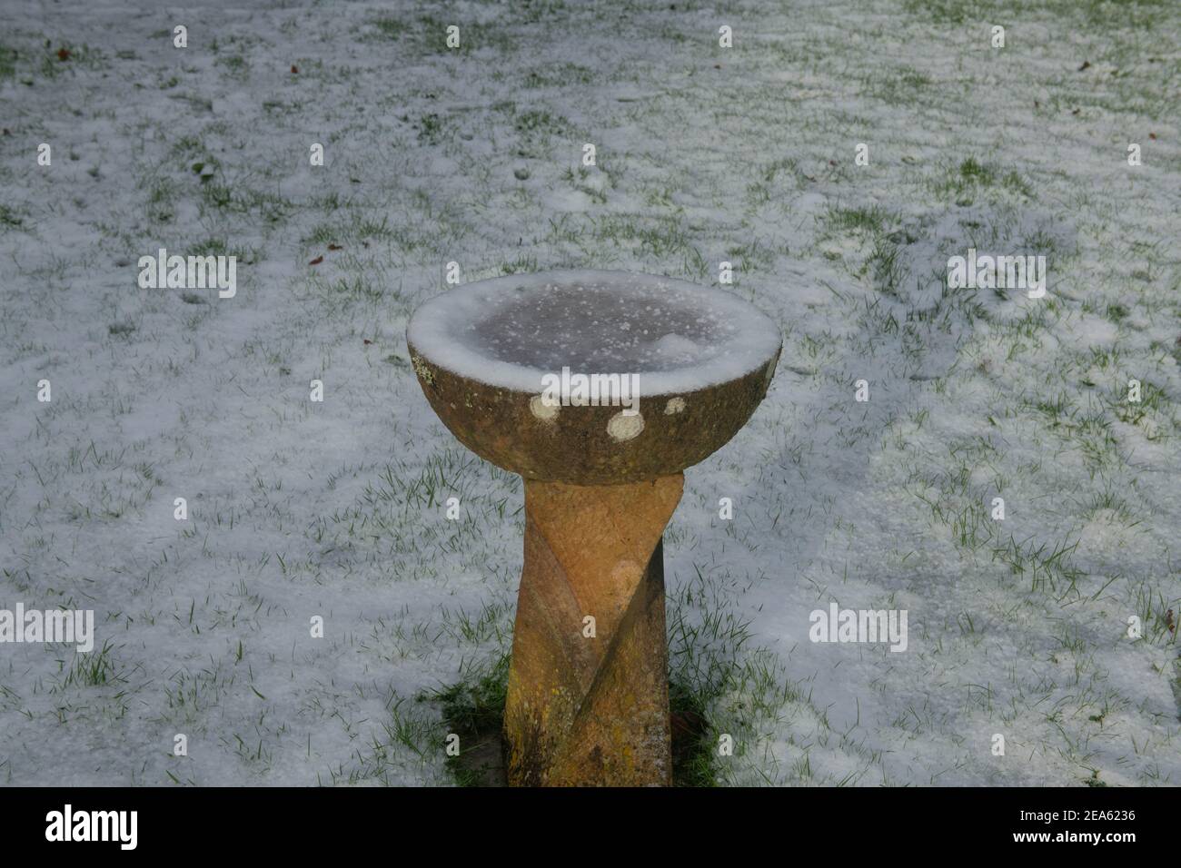 Frozen Water in a Stone Bird Bath Surrounded by Snow in a Country Cottage Garden in Rural Devon, England, UK Stock Photo
