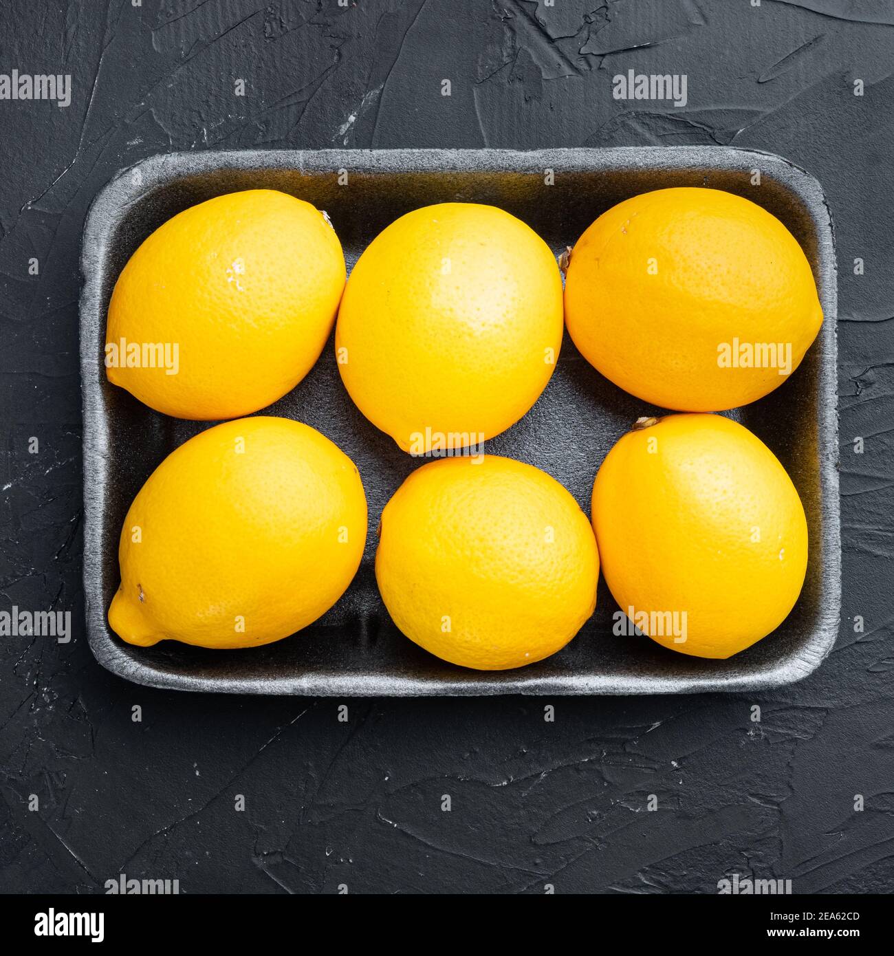 Ripe lemons set, in plastic tray, on black background, top view flat ...