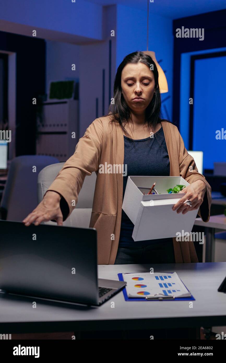 Depressed employee after being fired with cardbox in hands. Sad woman holding her belongings late at night in the office after being dismissed from job. Fired businesswoman, economy crisis Stock Photo