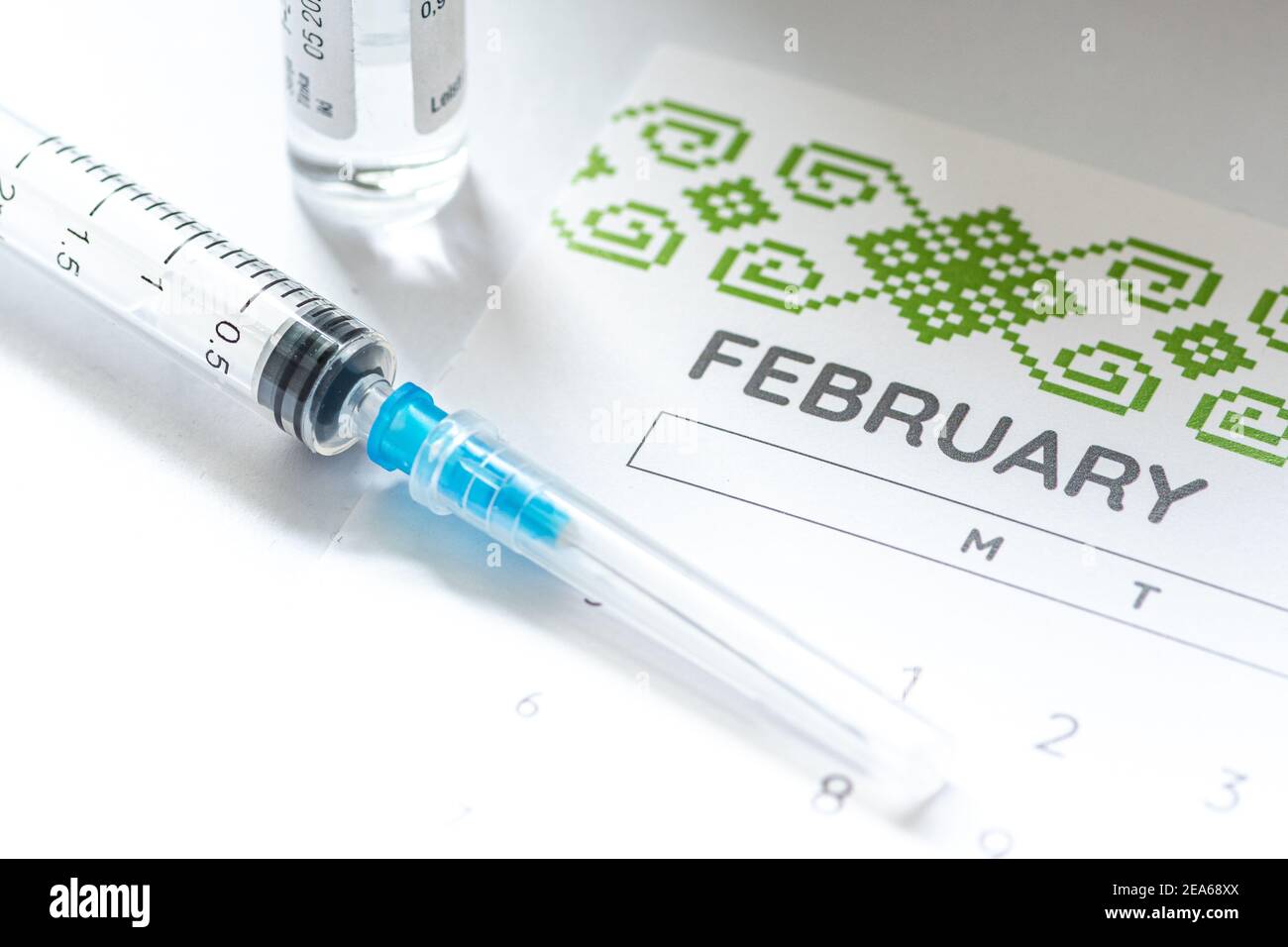 Syringe, glass vial or phial and calendar with month of February on a white table ready to be used. Covid or Coronavirus vaccine background, close up Stock Photo