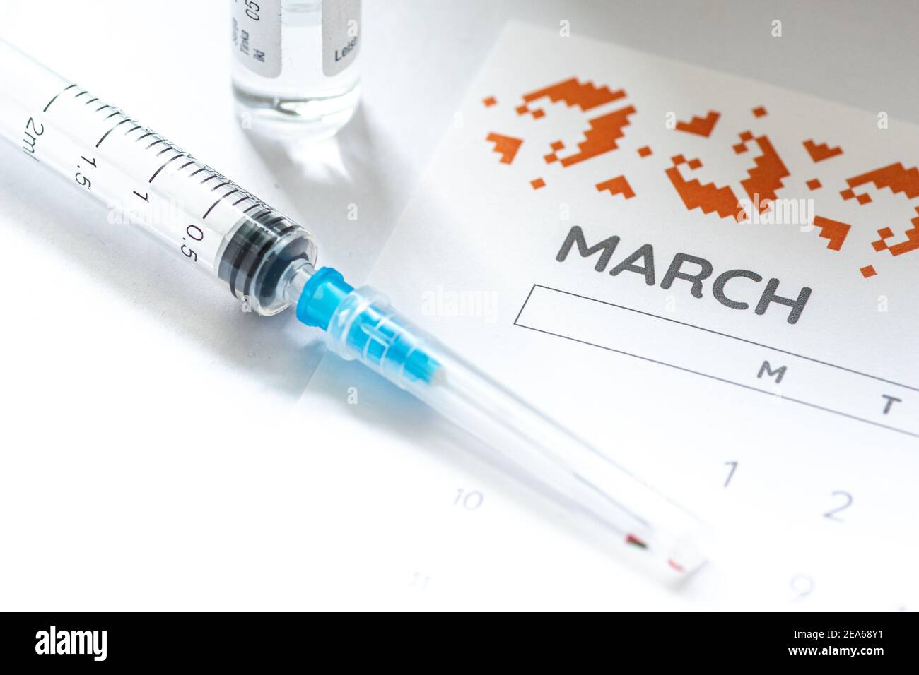Syringe, glass vial or phial and calendar with month of March on a white table ready to be used. Covid or Coronavirus vaccine background, close up Stock Photo