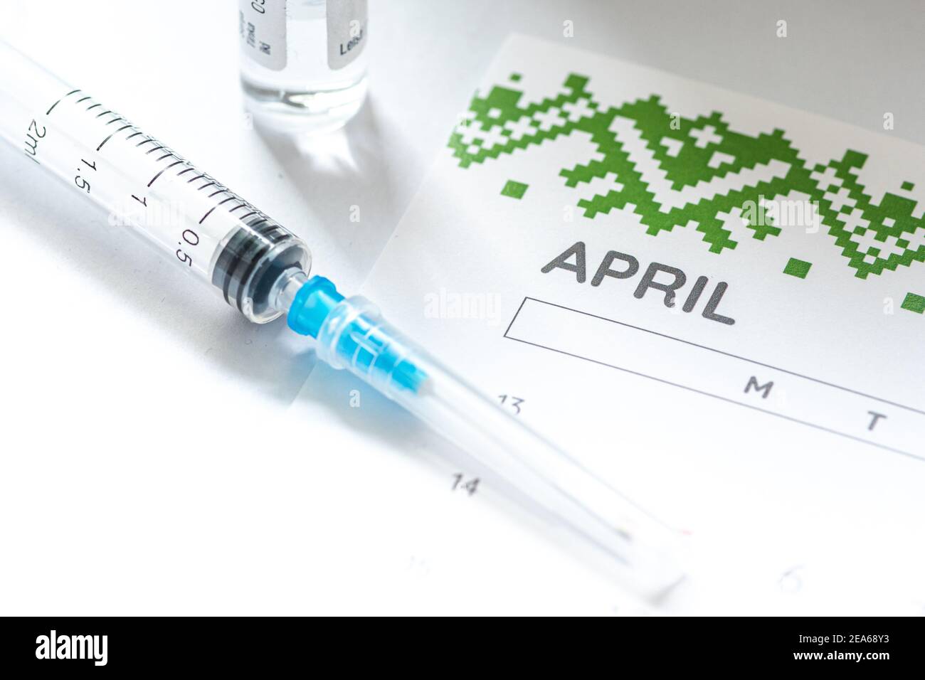 Syringe, glass vial or phial and calendar with month of April on a white table ready to be used. Covid or Coronavirus vaccine background, close up Stock Photo