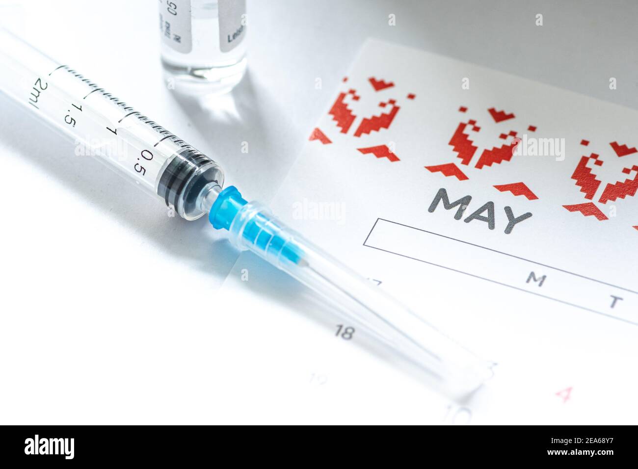 Syringe, glass vial or phial and calendar with month of May on a white table ready to be used. Covid or Coronavirus vaccine background, close up Stock Photo