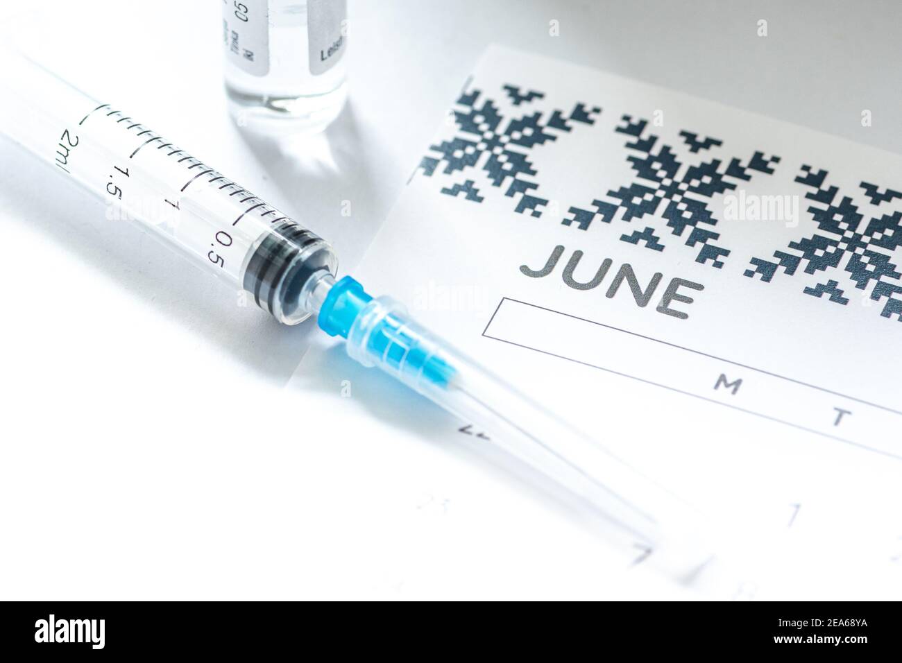 Syringe, glass vial or phial and calendar with month of June on a white table ready to be used. Covid or Coronavirus vaccine background, close up Stock Photo
