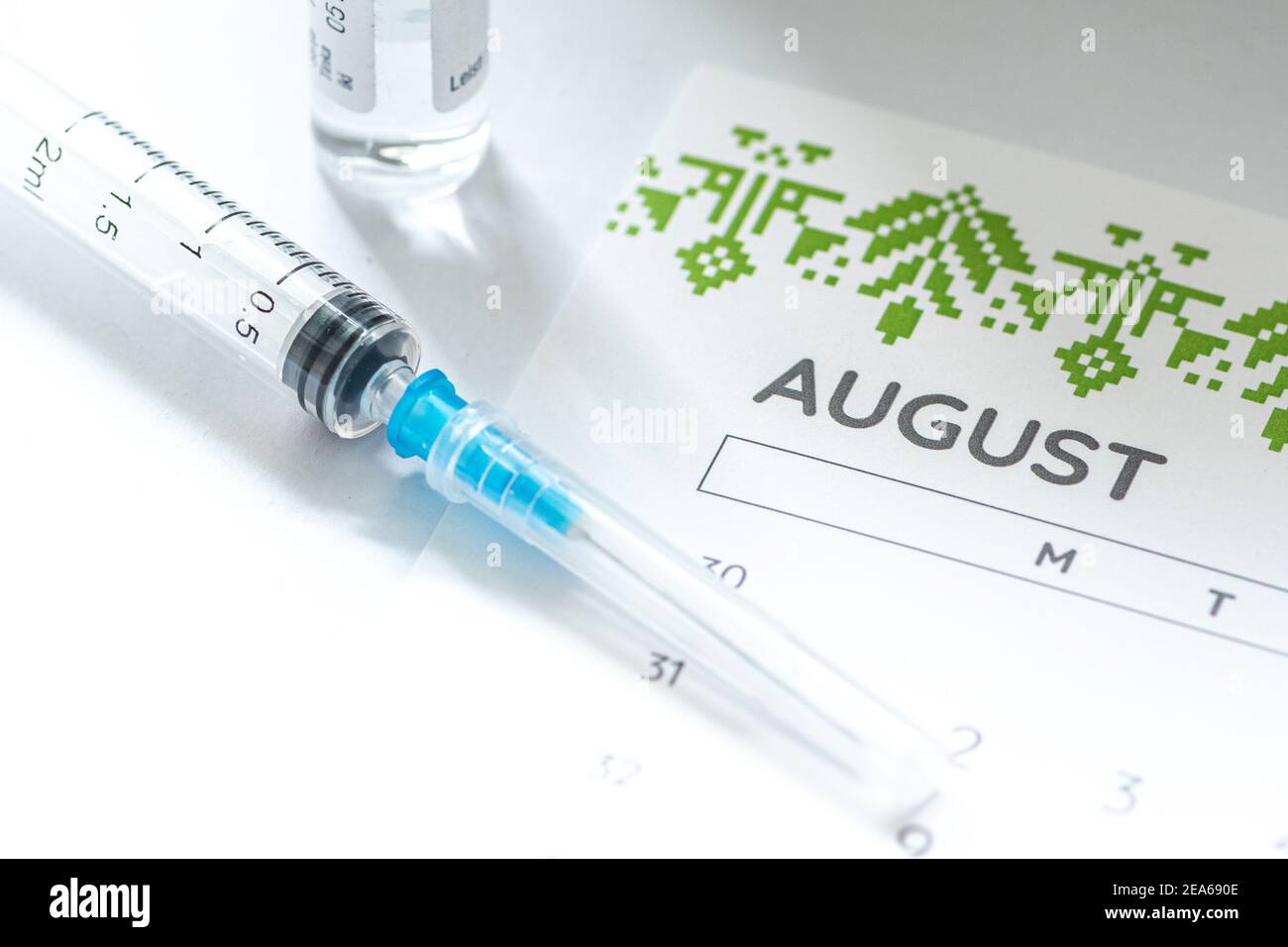 Syringe, glass vial or phial and calendar with month of August on a white table ready to be used. Covid or Coronavirus vaccine background, close up Stock Photo