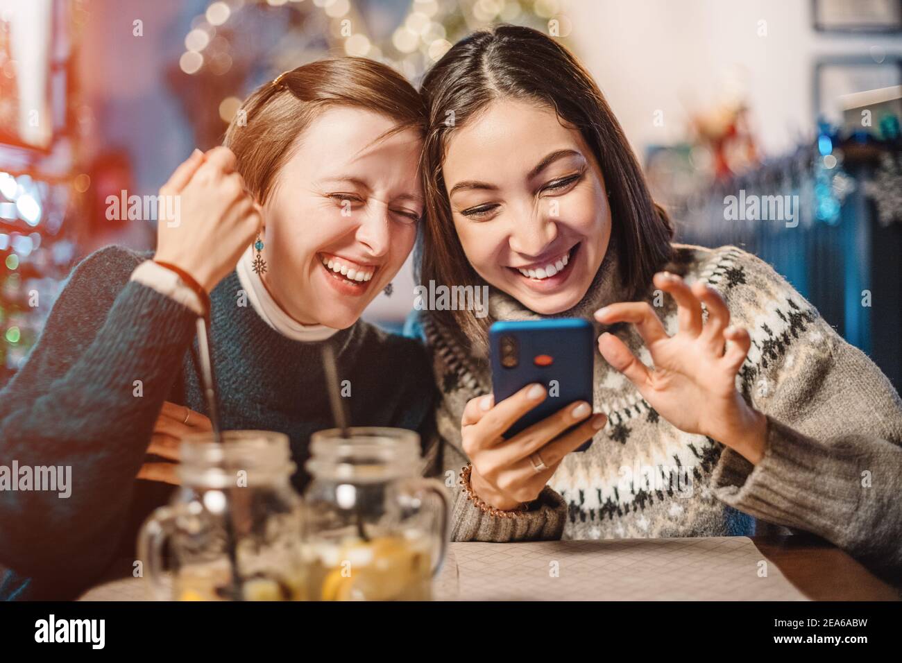 Two funny female friends look at new memes on social networks and laugh out loud in cafe. Smartphone with online Internet access - a new type of leisu Stock Photo