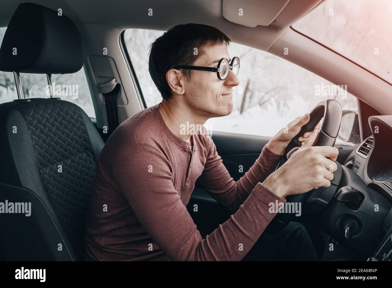 The ridiculous and idiotic nerd driver is staring at the road and holding the steering wheel. Concept of a novice driver and learning to drive in the Stock Photo