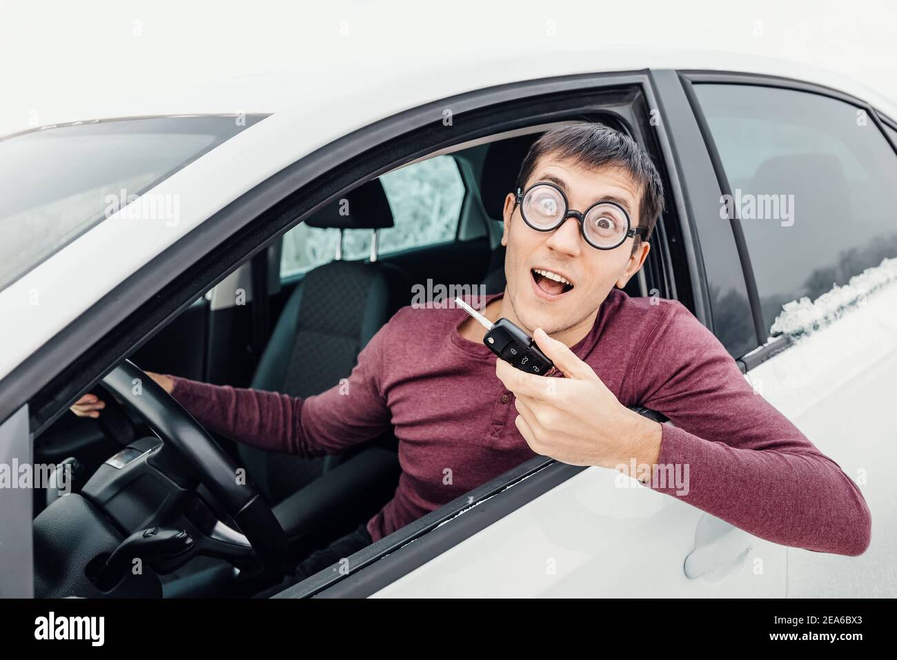 Funny driver in eye glasses holding the car key and smiling to the camera. Concept of a newbie driver and insurance Stock Photo