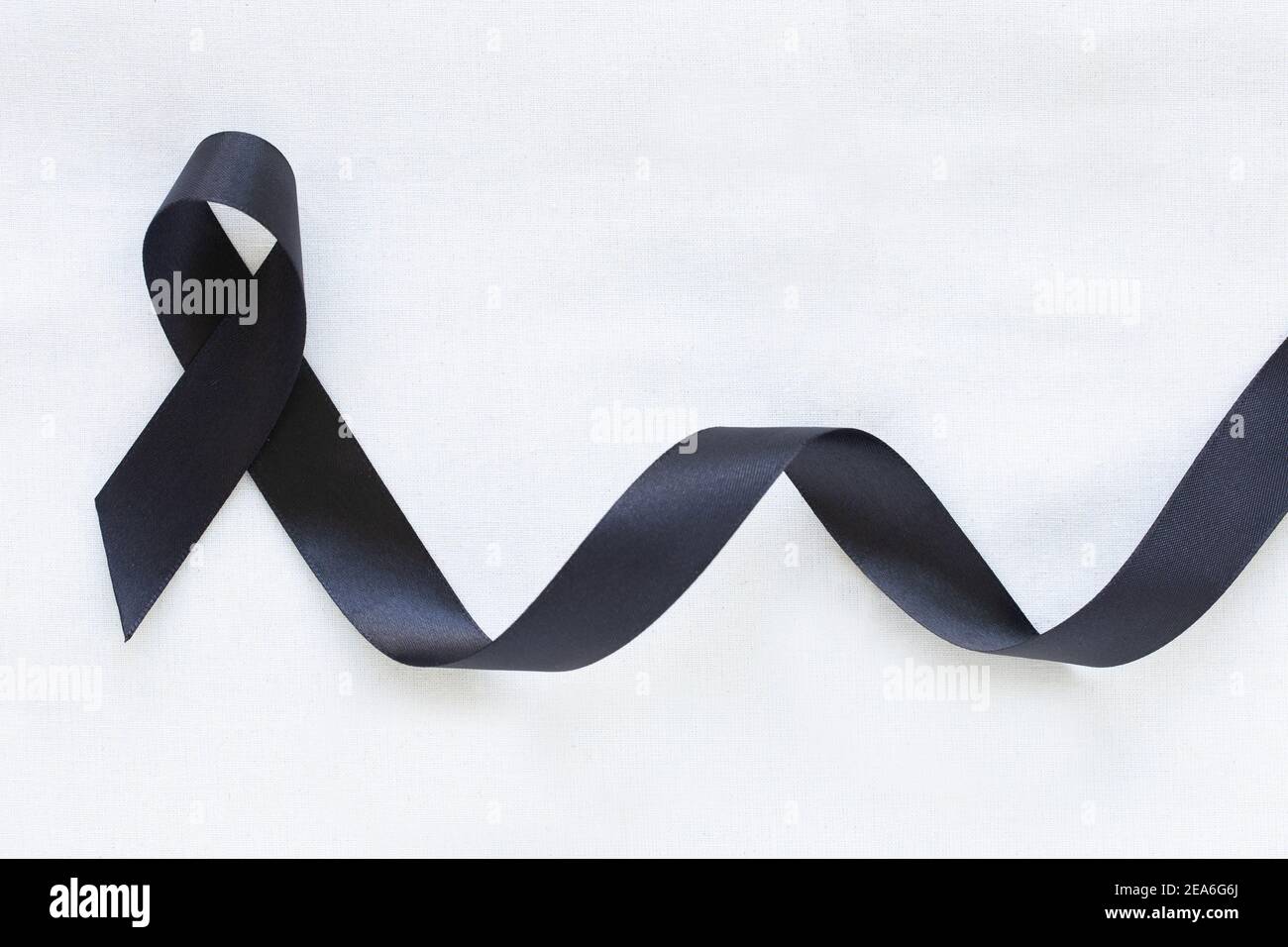 Black ribbon curl on white fabric background with copy space, symbol of Skin Cancer awareness month on May, Melanoma cancer, Mourning ribbon symbolic. Stock Photo