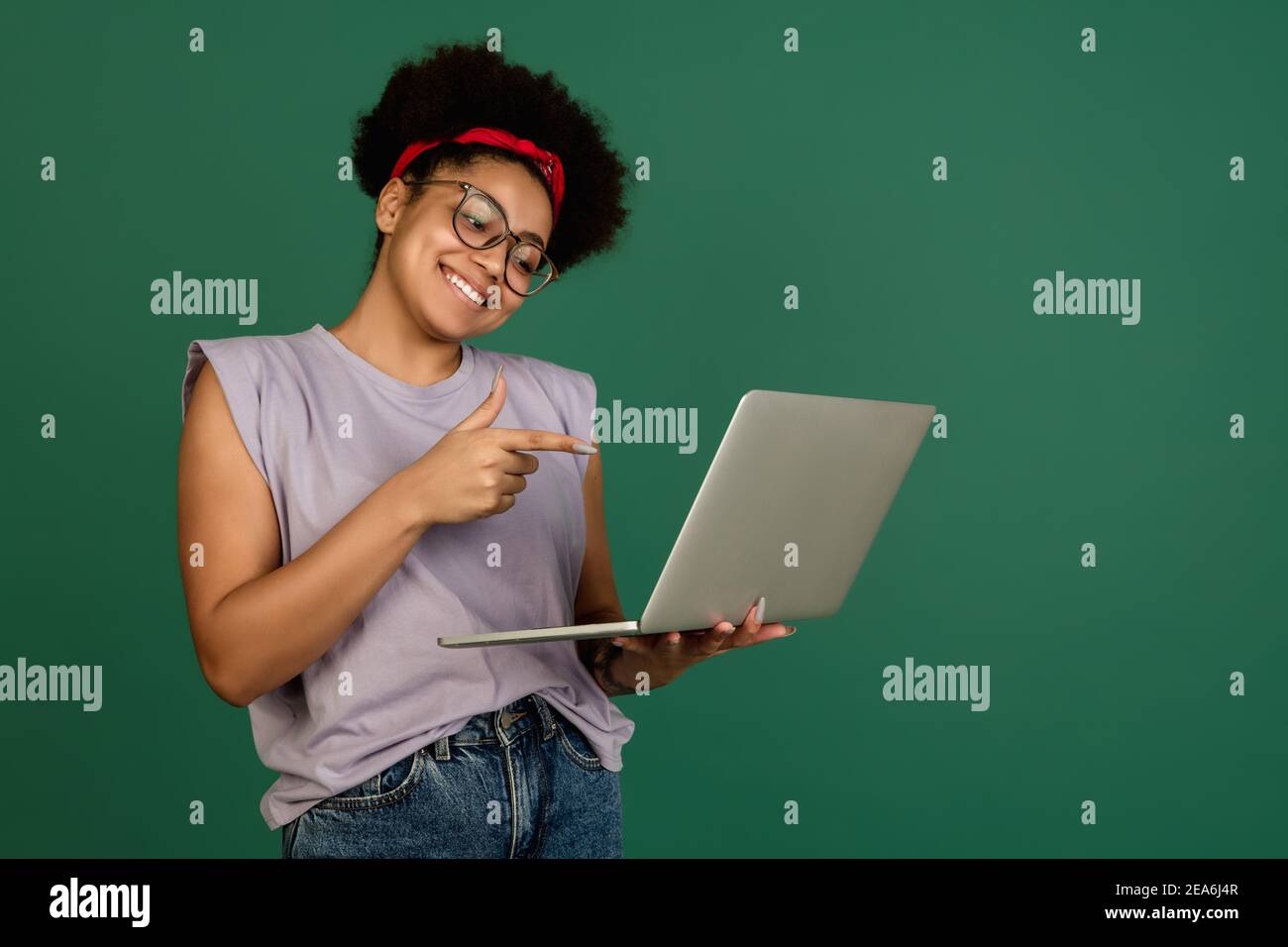Pointing. African-american beautiful woman's portrait isolated on green studio background with copyspace. Female model with laptop. Concept of human e Stock Photo