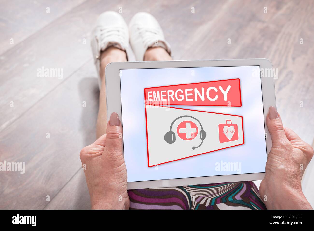 Woman sitting on the floor with a tablet showing emergency concept ...