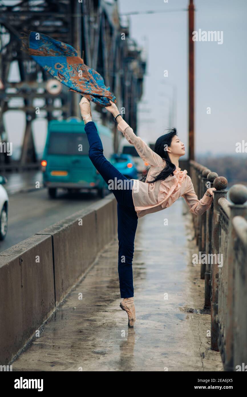 Japanese ballerina performs ballet arabesque pose on the bridge against the  background of road, cars and sidewalk with railings in rain Stock Photo -  Alamy