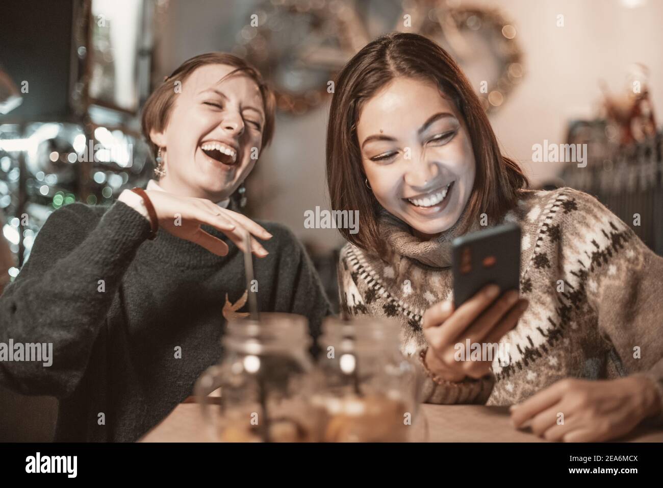 Two funny female friends look at new memes on social networks and laugh out loud in cafe. Smartphone with online Internet access - a new type of leisu Stock Photo