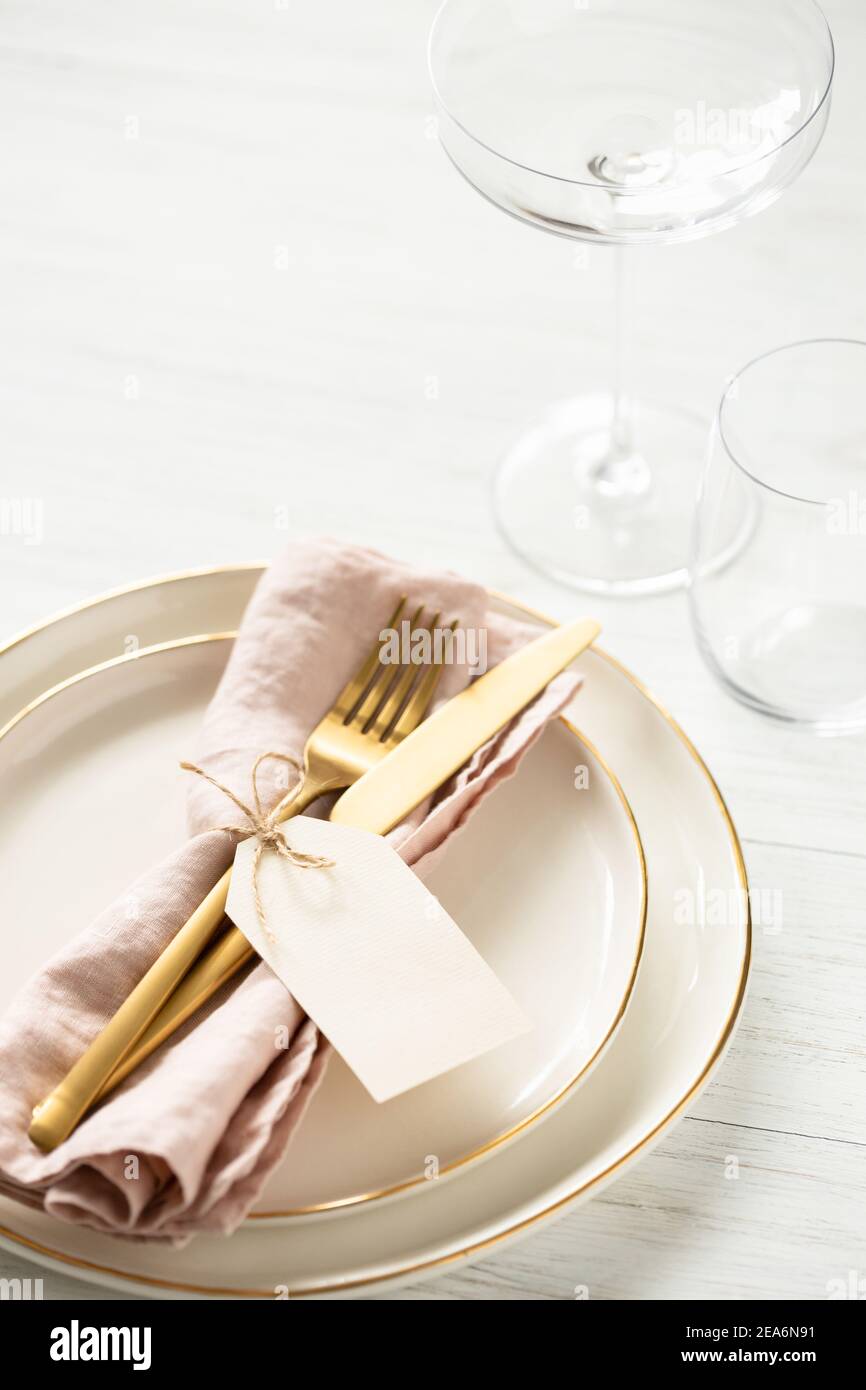 Golden rim plates and golden cutlery tied with blank tag on white table. Angle view on table setting. Stock Photo