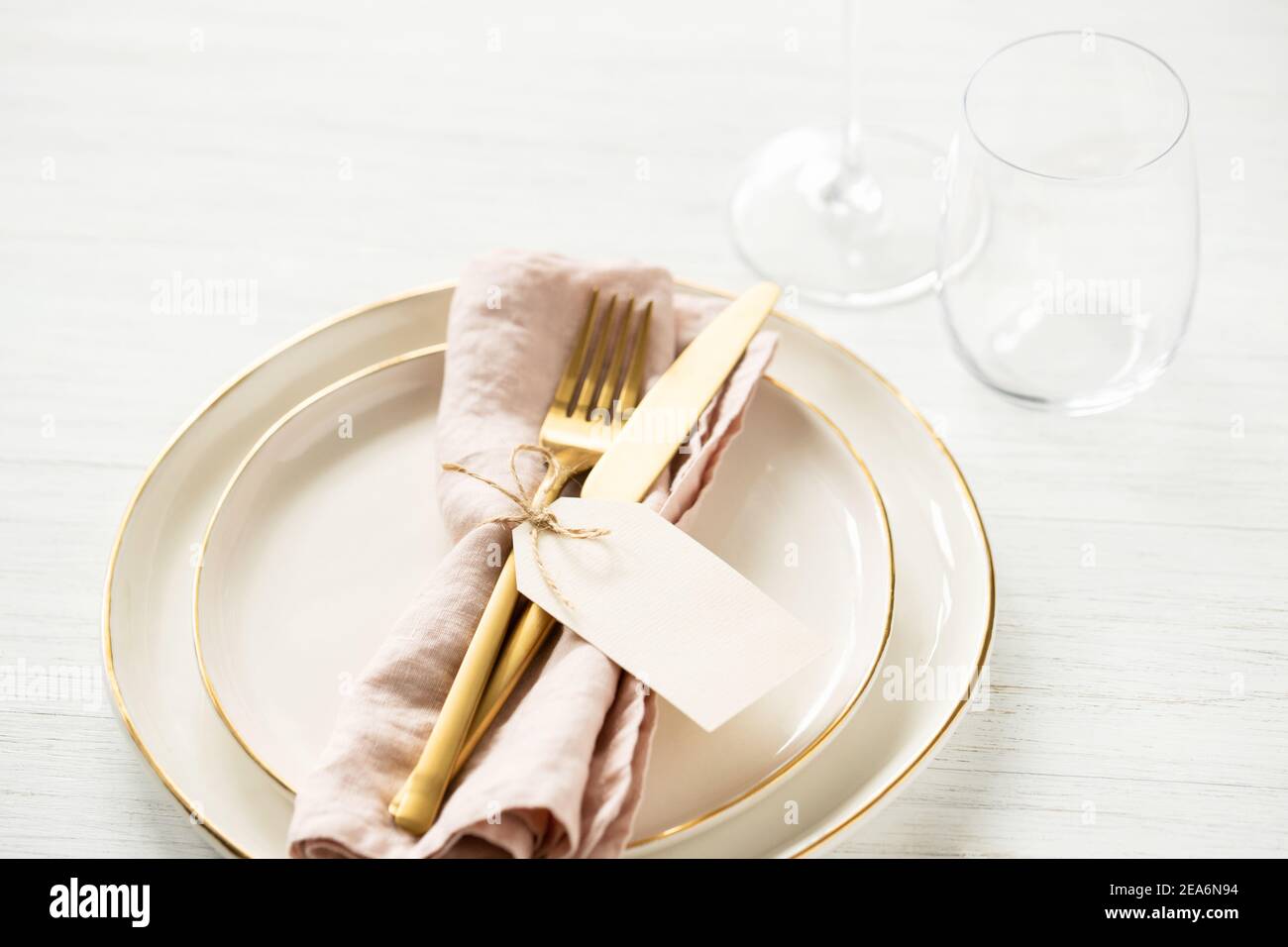 Golden rim plates and golden cutlery tied with tag on white table. Angle view on table setting. Stock Photo