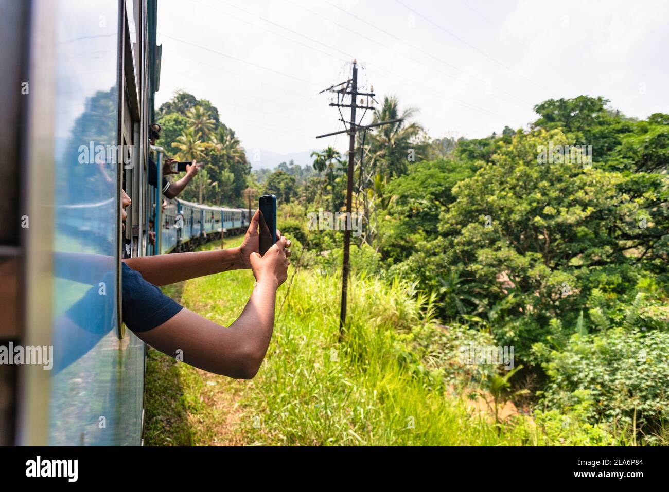 Man holding arm and taking phoot outside a Train of the Sri Lanka Railway, Scenic train journey through lush green forest in the hills Stock Photo